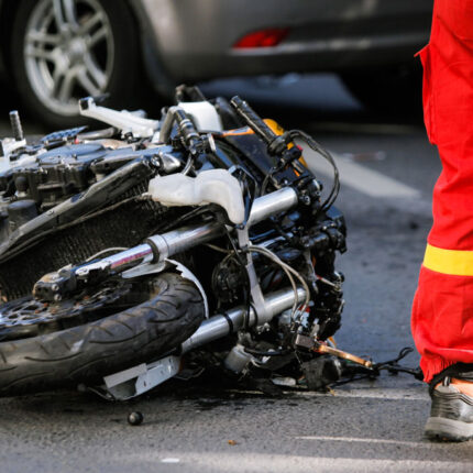 motorcycle on its side after accident with a vehicle with rider in reflective gear standing next to motorcycle Ridder Law Denver Colorado